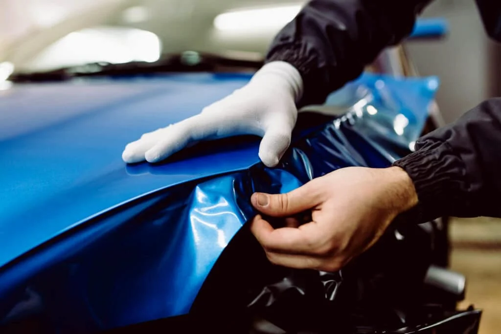 Professional applying blue wrap to a car's hood