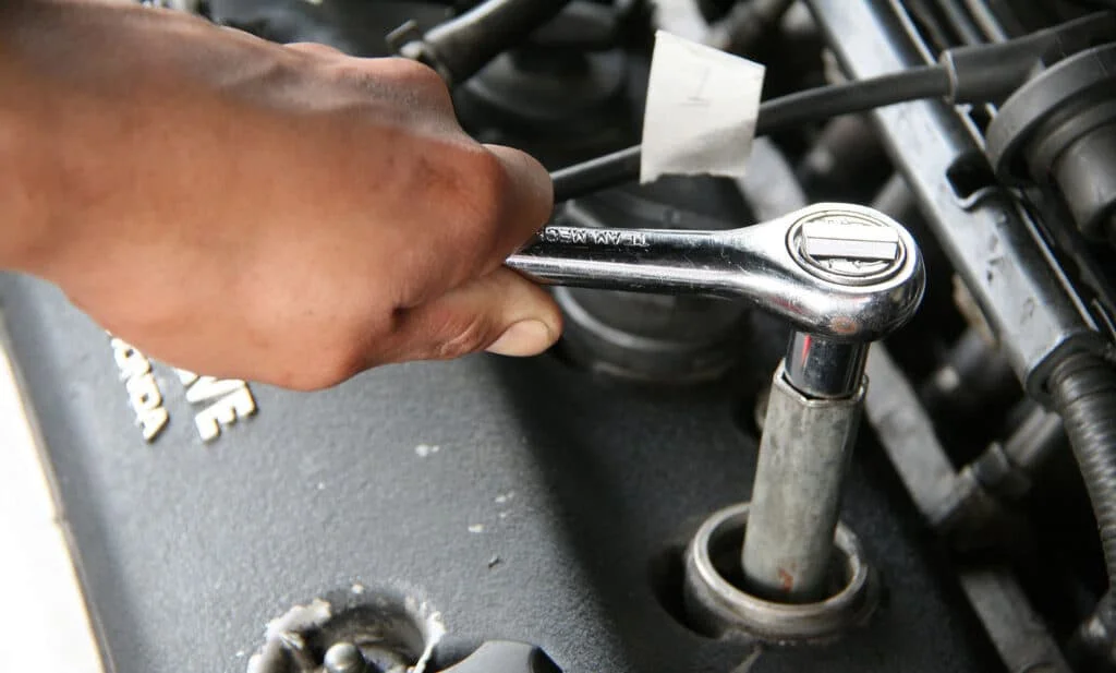 Person uninstalling spark plugs with a ratchet