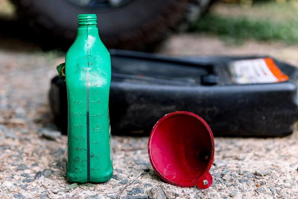 Old, unopened bottle of motor oil next to an oil pan and a red funnel