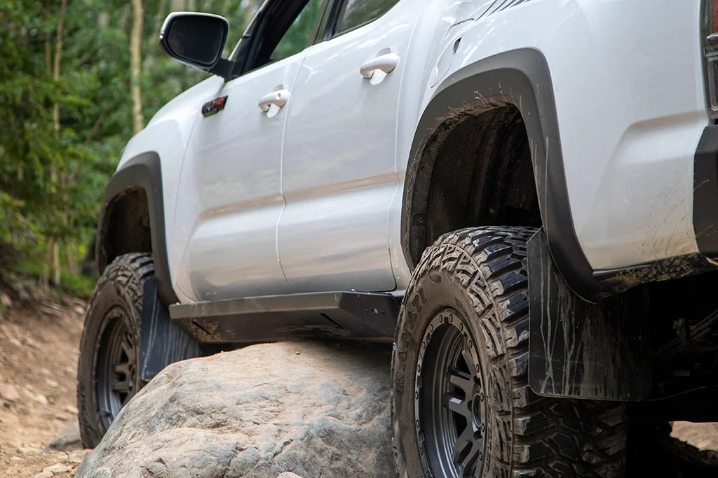 Tacoma equipped with rock sliders driving over a boulder