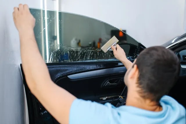 A professional applying window tint with a tool